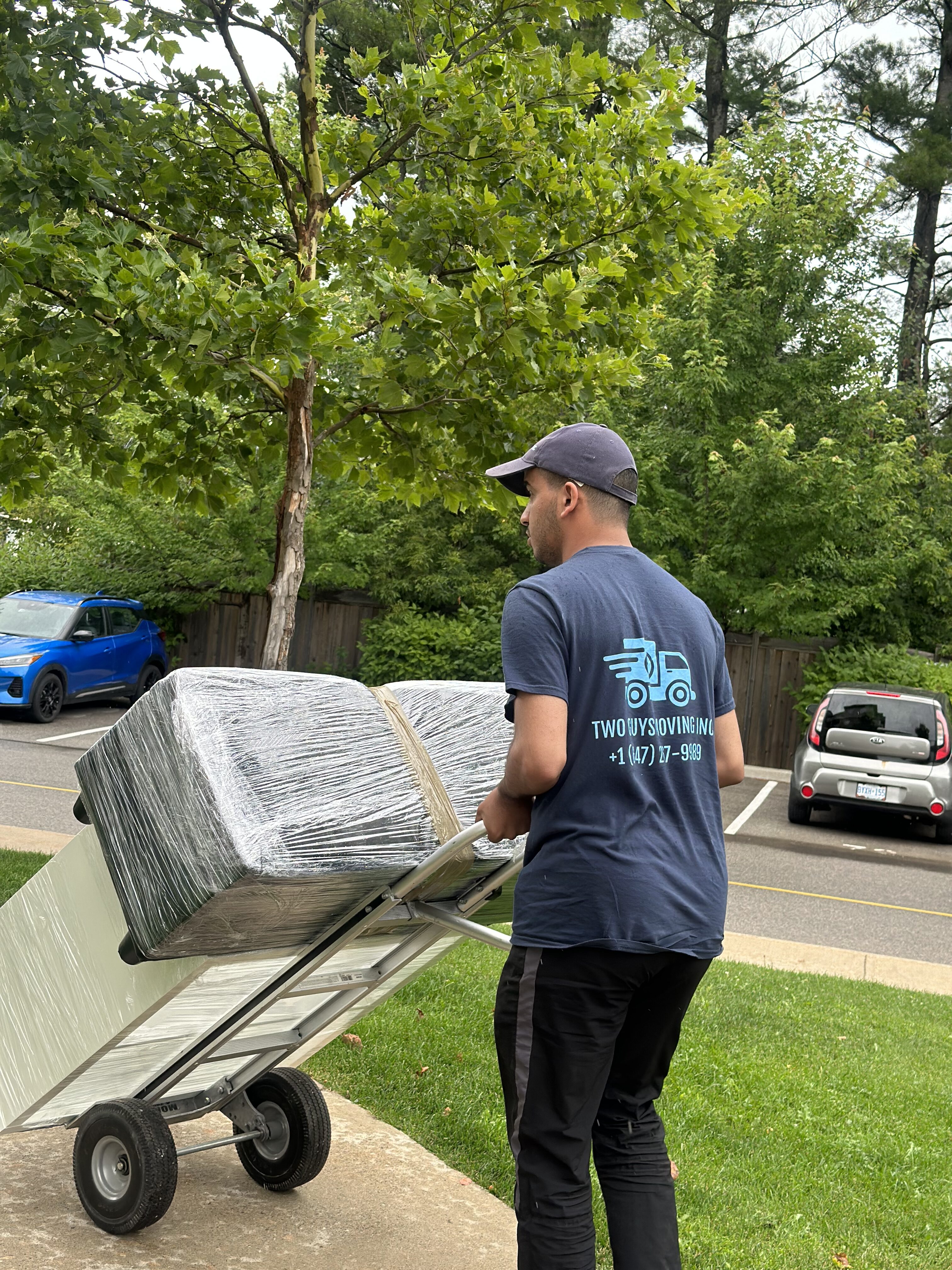 A mover with two guys moving shirt carrying some furniture in a dolly