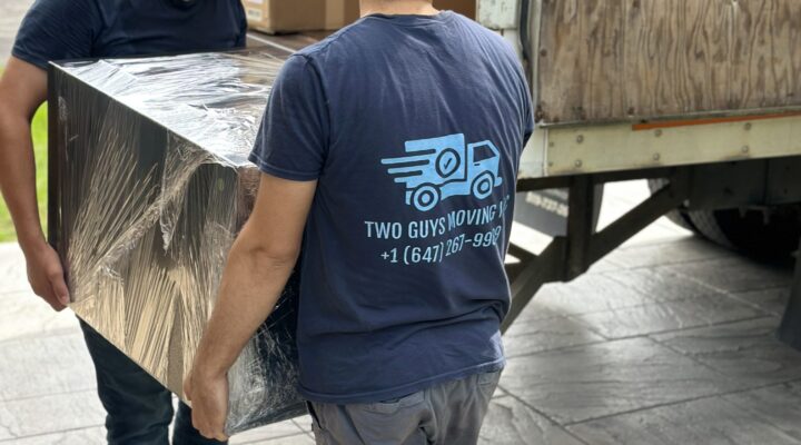 two movers loading shrink wrapped dresser to a truck