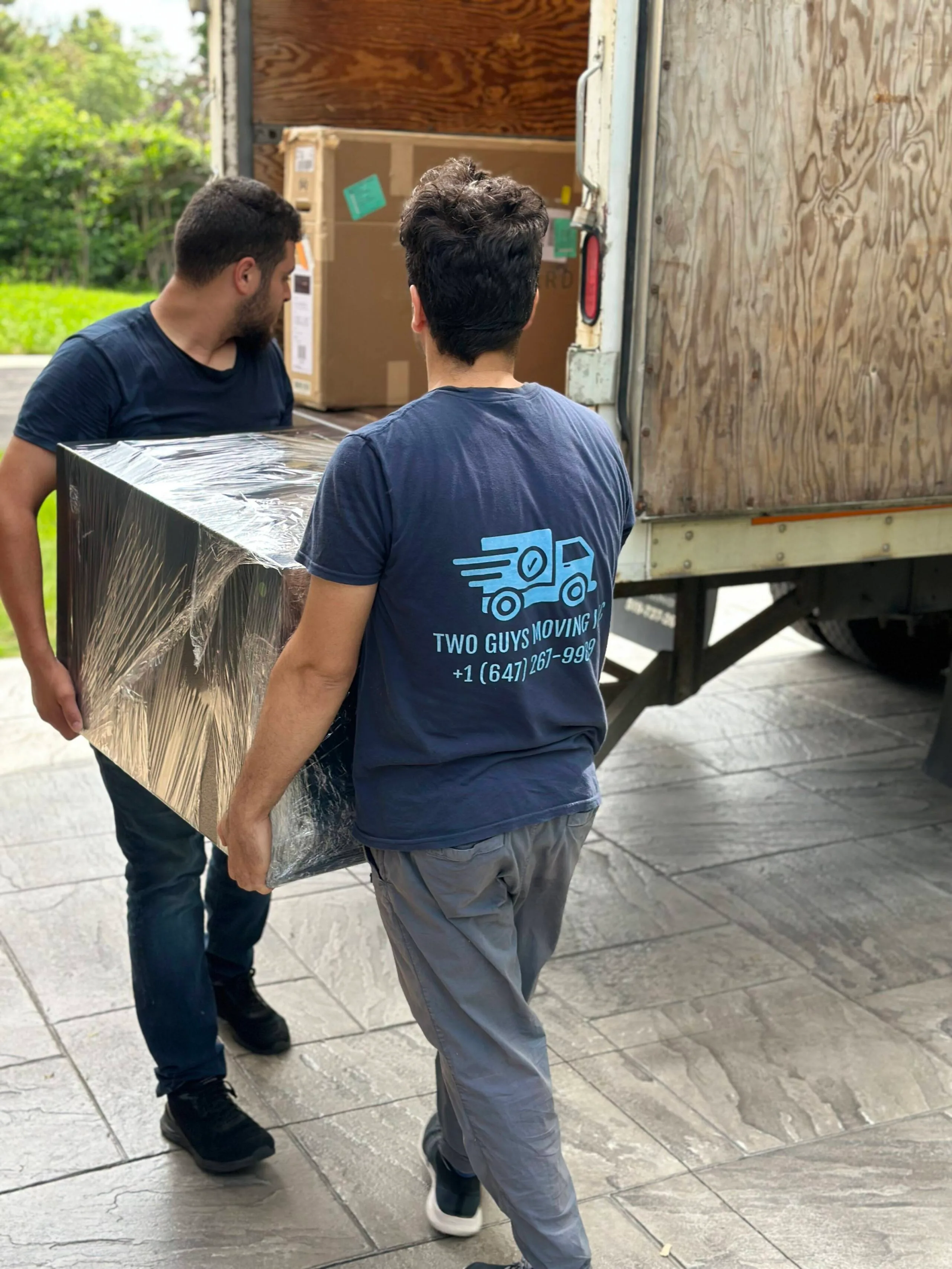 two movers loading shrink wrapped dresser to a truck